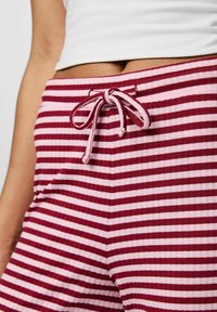 Röda och rosa randiga pyjamasshorts med dragsko i midjan. Tyget verkar mjukt med en ribbad struktur och sidofickor.