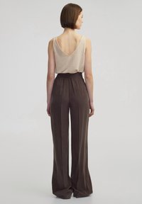Béžový top bez rukávů s V-výstřihem, doplněný o kalhoty s vysokým pasem, volné, tmavě hnědé, s hladkou texturou a širokými nohavicemi.