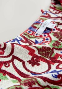 Tissu à motifs multicolores avec des tourbillons rouges, bleus, verts et blancs, présentant une finition texturée ; comprend une étiquette marquée "NEXT."