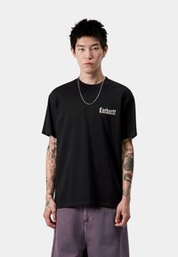 Camiseta de algodón negra con un pequeño logo blanco en el lado izquierdo del pecho. Mangas cortas, corte holgado, cuello redondo, con una textura suave.