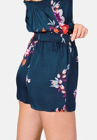 Shorts fleuris en tissu bleu marine, dotés d'une taille élastique et de motifs de fleurs vives en rose, orange et bleu canard. Coupe fluide avec fentes sur les côtés.