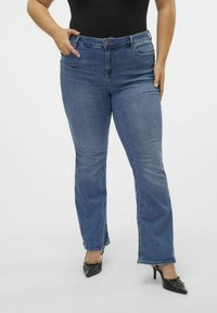 Blue straight-leg jeans made of denim with a front button closure, belt loops, and two front pockets, worn with black high-heeled shoes.