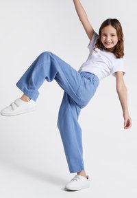 Jasnoniebieskie szerokie spodnie wykonane z denimu, z tylną kieszenią, w połączeniu z białą koszulką z krótkim rękawem i białymi trampkami.