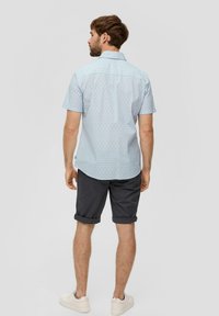 Korte mouw lichtblauw shirt met een geometrisch patroon, gecombineerd met donkere opgerolde shorts en witte sneakers, gezien vanuit de achterkant.