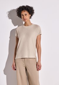Beige textured t-shirt with short sleeves and a crew neckline, paired with beige wide-leg pants, set against a light background.