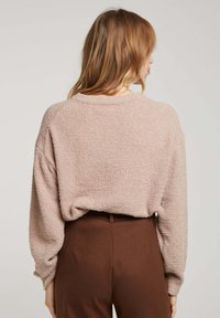 Pull rose texturé avec une coupe décontractée, un col rond et des épaules tombantes, associé à un pantalon marron taille haute.