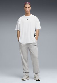 T-shirt blanc à manches courtes avec logo noir, associé à un pantalon de survêtement gris clair avec le texte "PUMA CREW", et des chaussures de sport de couleur claire.