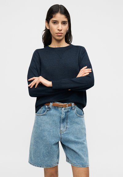 Πουλόβερ σε ναυτικό μπλε με μακριά μανίκια και στρογγυλή λαιμόκοψη, συνδυασμένο με σορτς από ανοιχτό μπλε τζιν και καφέ ζώνη, με μπροστινές τσέπες.