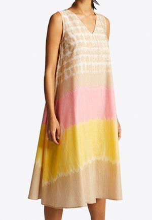 Sukienka midi bez rękawów z dekoltem w serek i wzorem tie-dye w kolorach beżowym, różowym i żółtym, noszona przez stojącą osobę z ramionami swobodnie opuszczonymi wzdłuż ciała.