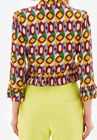 Farverig bluse med mønstre, der har geometriske designs i rød, grøn, gul og blå, med flæser på ærmerne og en peplum-iskant.