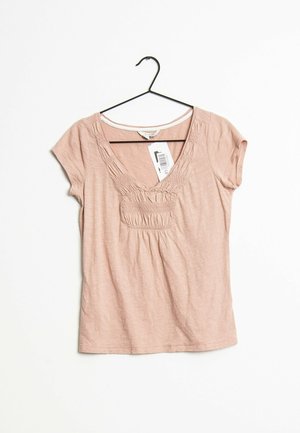 Top para mujer de manga corta en color rosa claro con detalle fruncido alrededor del escote en V, colgado en una percha negra contra un fondo blanco con etiqueta de precio visible.