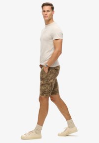 Lichtbeige T-shirt met korte mouwen, gecombineerd met cargoshorts in camouflagepatroon, met zijzakken en een casual pasvorm. Beige sneakers met getextureerde sokken.