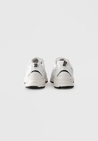 Baskets de sport blanches avec des accents noirs vues de l'arrière sur un fond blanc uni.