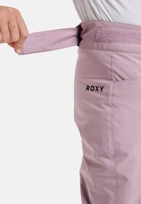 Lichtroze broek met een klittenband tailleverstelling. Geborduurd "ROXY" logo op de achterkant. Glad materiaal met een getailleerde pasvorm.
