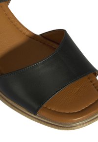 Schwarze Ledersandale mit einem breiten oberen Riemen, braunem Fußbett und strukturierter Laufsohle. Dezente Steckdetails verbessern das Design.
