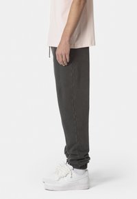 Dunkelgraue Sweatpants mit elastischen Bündchen, lockerer Passform, getragen mit weißen Sneakern, die über strukturierte Schnürsenkel und gerippte Socken verfügen.