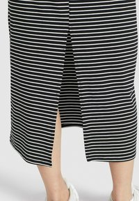 Randig kjol i svart och vitt med en slits bak, som visar underbenen och vita sneakers mot en enfärgad bakgrund.