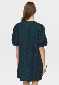 Mörkblå puffärmad klänning med blommönster, texturerad tyg och rak skärning, som har rund halsringning och en detalj med söm bak.
