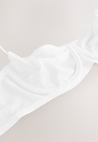 Baltos spalvos liemenėlė iš lengvos tinklelio medžiagos, su lygiomis kontūromis, reguliuojamais dirželiais ir besiūliu dizainu su minkšta elastine juosta.