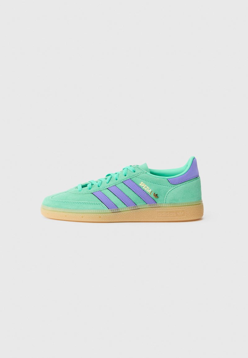 Green suede sneaker with purple stripes, rubber gum sole, and gold logo detail. Rounded toe and flat laces for secure fit.