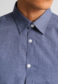 Korte mouwen, knoopschaal shirt van gestructureerde donkerblauwe stof met een klassieke kraag en twee witte knopen nabij de hals, met een geweven patroon.
