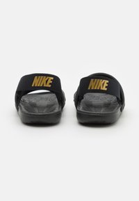 Černé ploché sandály z materiálu s texturovanou podrážkou, textilními pásky se zlatým logem Nike, plochý design a žádné další akcenty nebo vzory.