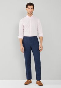 Lichtroze geblokte overhemd met knoopjes, gecombineerd met donkerblauwe op maat gemaakte broek. Bruine suède instappers maken de outfit af. Soepele texturen en getailleerd ontwerp.