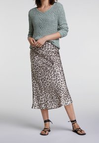Suéter de punto verde claro con un patrón texturizado, combinado con una falda midi de seda con estampado de leopardo y sandalias negras con tiras.