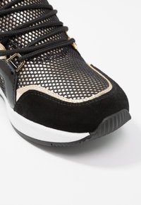 Czarno-złote buty sportowe z siateczkową cholewką, zamszowymi akcentami i czarnymi sznurówkami; posiadają białą podeszwę środkową oraz teksturowaną gumową podeszwę zewnętrzną.