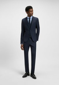 Merimiespuku, jossa on räätälöity muotoilu, yhteensopivat housut ja vaaleansininen paita. Mustat nahkakengät täydentävät virallista asua.