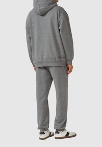 Grauer Sweatshirt und passende Hose aus weichem Material. Der Kapuzenpullover verfügt über eine Kordel und gerippte Bündchen; die Schuhe sind weiß mit dunklen Akzenten.