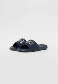 Papuci de plajă de culoare albastru închis, din cauciuc, cu o curea lată pe care este inscripționat cuvântul „NIKE” în argintiu reflexiv. Talpa texturată oferă aderență.