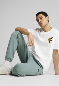 Hvid bomulds T-shirt med en gul og sort grafisk design, parret med lysegrønne sporty joggers med elastiske manchetter og logo detaljer.