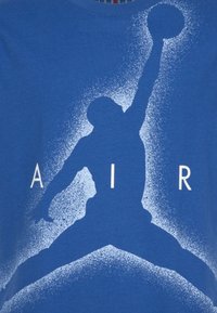 Silueta basketbalisty skákajícího s jednou rukou nataženou a držícím míč, obklopeného textem "AIR" na modré tkanině.