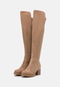 Botas de ante color beige hasta la rodilla con un acabado texturizado, tacón en bloque, punta redondeada y detalles en las costuras laterales. Cuenta con una suela de goma para mayor tracción.