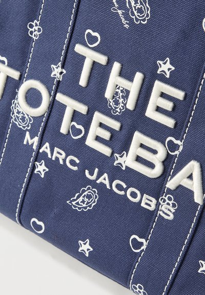 Zbliżenie na granatową torebkę z teksturowanej tkaniny z białym haftem "THE TOTE BAGS MARC JACOBS" oraz białymi wzorami paisley, gwiazdek i serc.