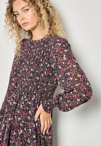 Kwiecista sukienka na czarnym tle, z różowymi i fioletowymi kwiatami. Marszczony górny część, długie rękawy i zwiewna spódnica.