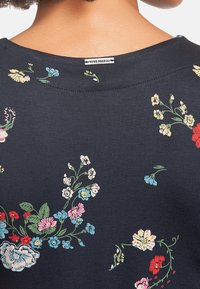 Marinblå bomullsplagg med blommönster i rosa, rött, gult och blått. Har en rundad halsringning och synlig varumärkesetikett "Vive Maria."