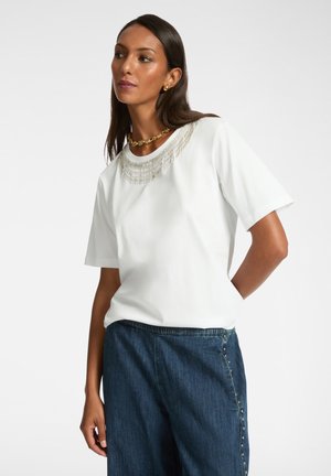 T-shirt blanc à manches courtes avec un col en perles, associé à un pantalon en denim bleu foncé. Tissu lisse avec une silhouette à coupe décontractée.