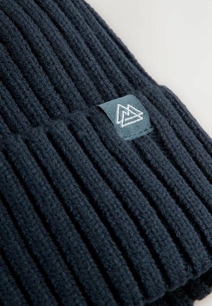 Écharpe tricotée bleu marine avec une texture côtelée, dotée d'une petite étiquette bleu clair avec un logo géométrique brodé sur un côté.