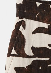 Beżowa tkanina z dużym, ciemnobrązowym, abstrakcyjnym kwiatowym wzorem oraz widocznym przeszyciem wokół kieszeni i pasa.