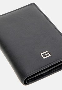 Portafoglio in pelle nera con superficie testurizzata, caratterizzato da un logo 'G' in argento e cuciture visibili lungo i bordi. Design pieghevole.