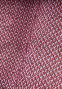 Tkanina z geometrycznym wzorem czerwonych i niebieskich trójkątów na strukturalnym tle, z równomiernie rozmieszczonymi trójkątnymi kształtami na całej powierzchni.