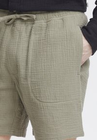 Shorts vert olive clair en tissu texturé, dotés d'une taille élastique avec cordon de serrage et de poches latérales.