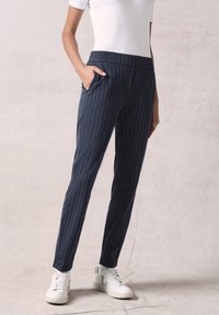 Marineblauwe gestreepte broek met een elastische tailleband, zijzakken en een slanke pasvorm. Gecombineerd met witte sneakers met subtiele blauwe accenten.