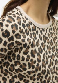 Top de estampado de leopardo con fondo crema y manchas marrones y negras. Textura suave y escote redondo con un ribete beige que contrasta.