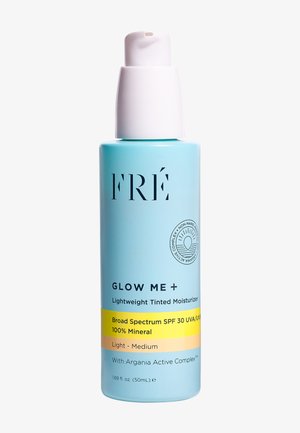 Bouteille bleu clair avec un bouchon-pompe blanc, étiquetée "FRÉ GLOW ME +". Contient 50 ml d'un hydratant teinté léger avec SPF 30.