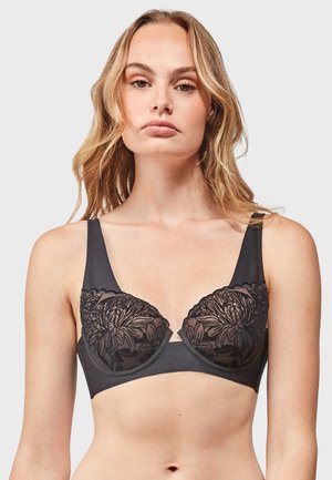 Black bra with sheer floral lace detailing on the cups, smooth fabric, wide straps, and a structured underwire design.
