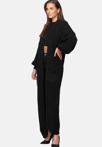 Lång svart stickad cardigan med oversized ärmar, framfickor och öppning fram. Tillverkad av strukturerad tyg, vilket ger en mysig känsla.