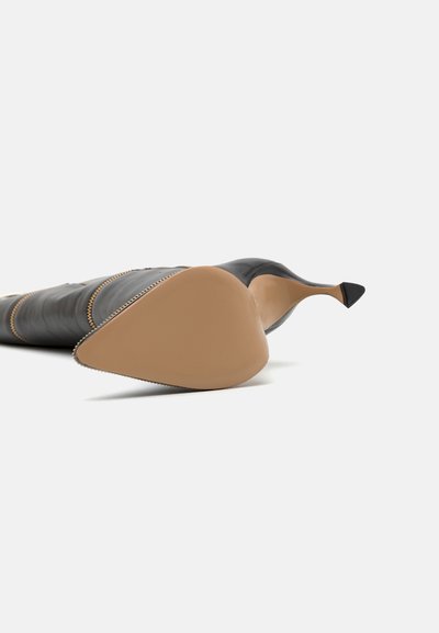 Zwarte leren hoge hak schoen met een spitse neus, voorzien van een gladde oppervlakte, beige zool en elegante stiksels langs de rand.